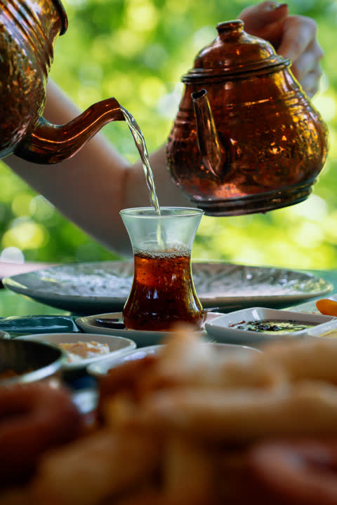 İnce belli bardağa demlik çay dökülürken
